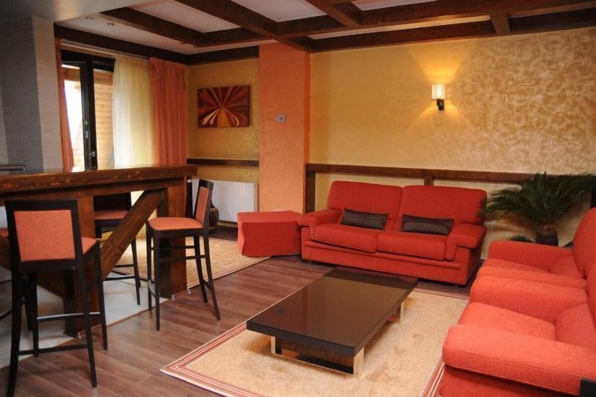 Un salon avec un canapé rouge, des chaises en bois, une table basse et une lampe fixée au mur.