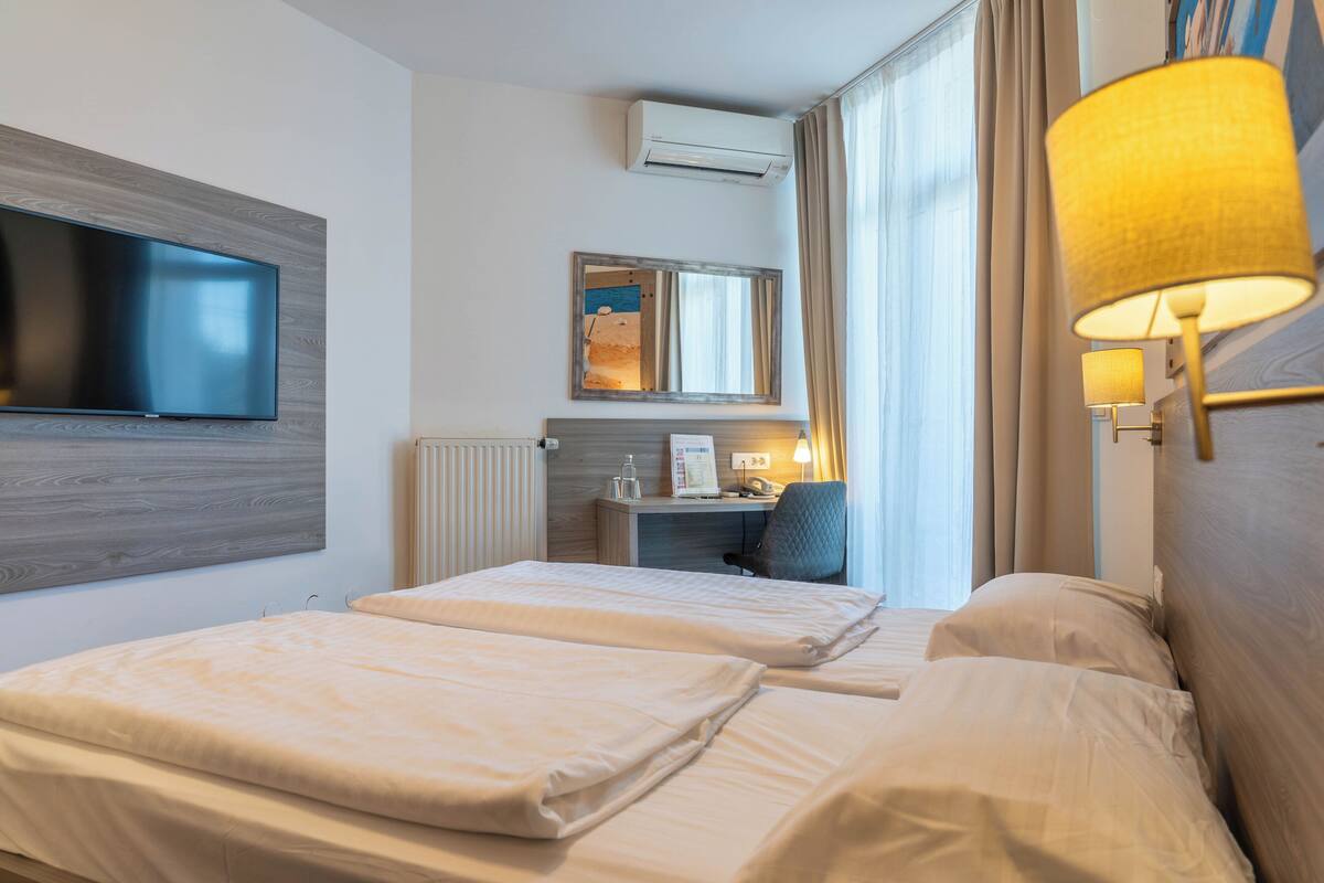 Une chambre d’hôtel avec deux lits, un téléviseur à écran plat fixé au mur, un bureau avec une chaise et une lampe.