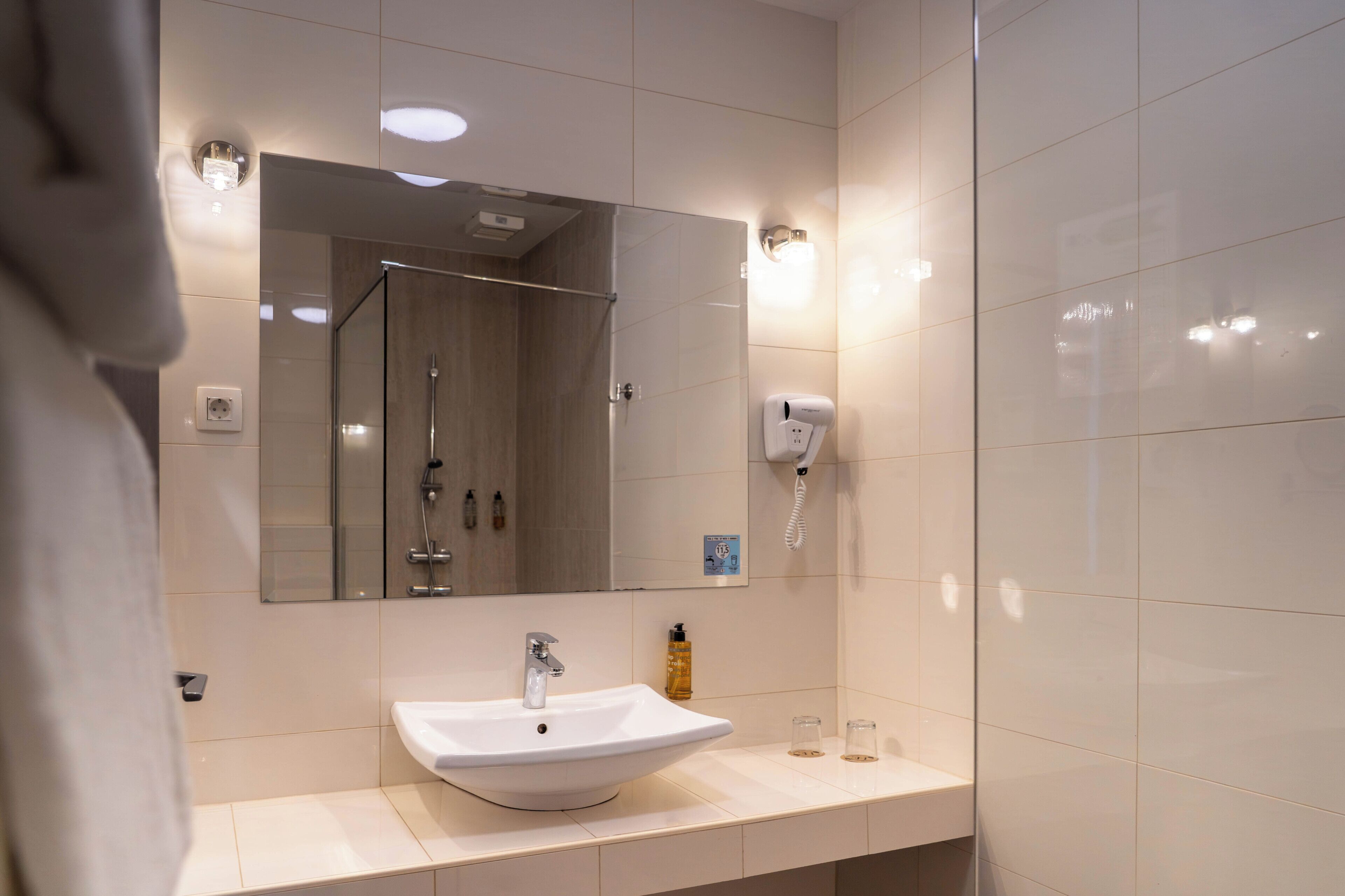 Ein modernes Badezimmer mit einem weißen Waschbecken, einem Spiegel, einer Handbrause und einem an der Wand montierten Telefon.
