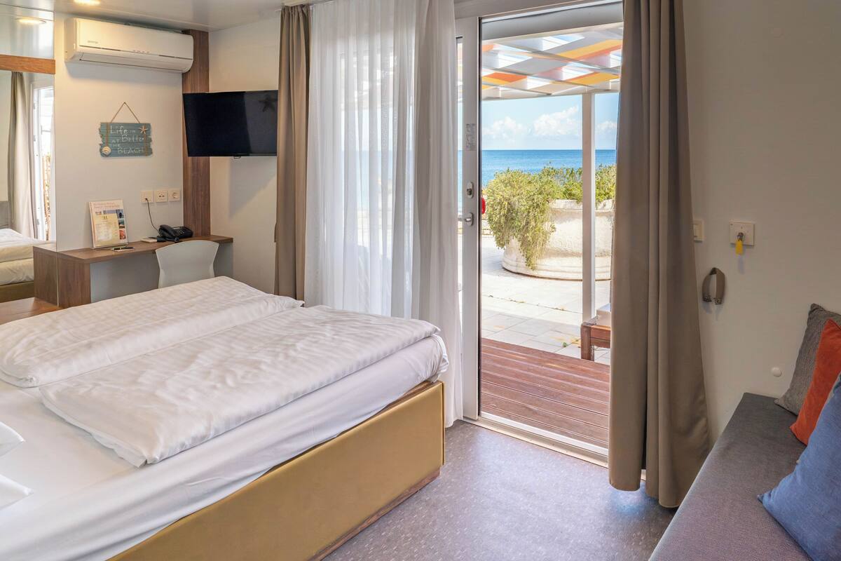 Une chambre d’hôtel avec un lit, un bureau, une télévision et un balcon donnant sur la mer.