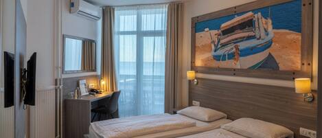 A hotel room with two beds, a desk, a chair, an air conditioning unit, a painting of a boat, and a window with curtains.