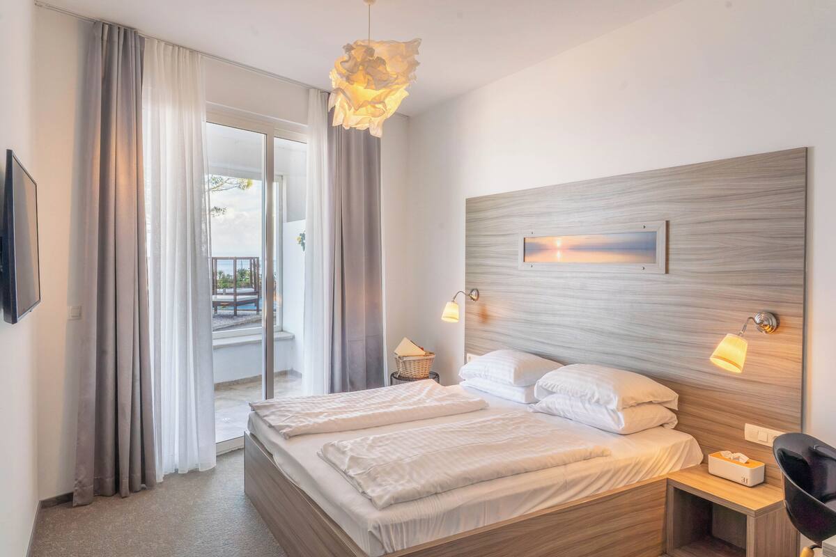 Une chambre d’hôtel avec un lit, deux lampes de chevet, une télévision, une fenêtre avec des rideaux et une vue sur l’extérieur.