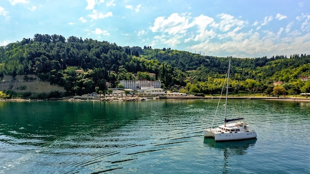 Ein ruhiger See mit einem Boot, das vor einem Gebäude mit einem Hügel im Hintergrund liegt.