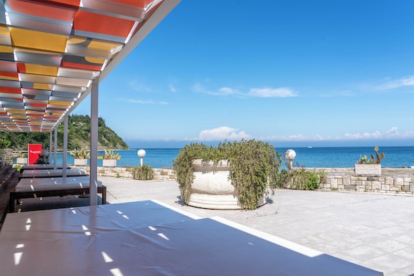 A covered outdoor seating area with a view of the sea, stone walls, and potted plants. - Barbara Piran Beach hotel (Piran)