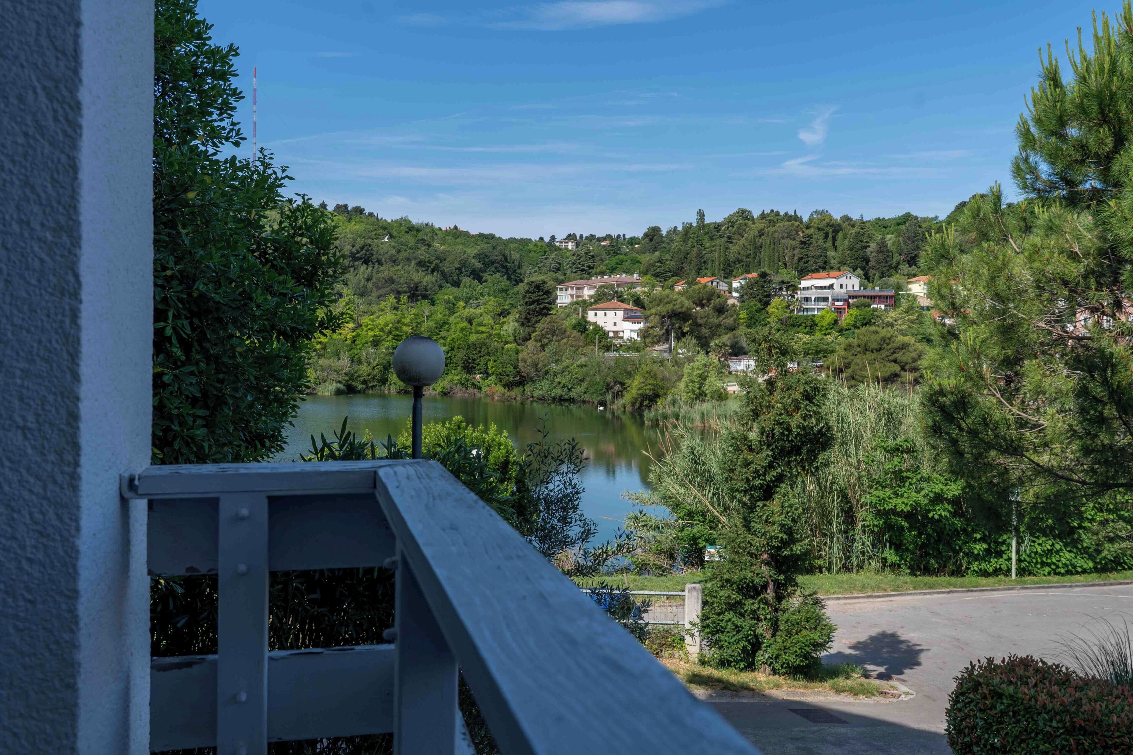 A lakeside view with a wooden deck, a lamp post, and houses in the background.