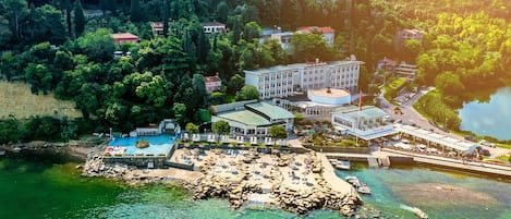 An aerial view of a coastal resort with a swimming pool, beach area, and several buildings.