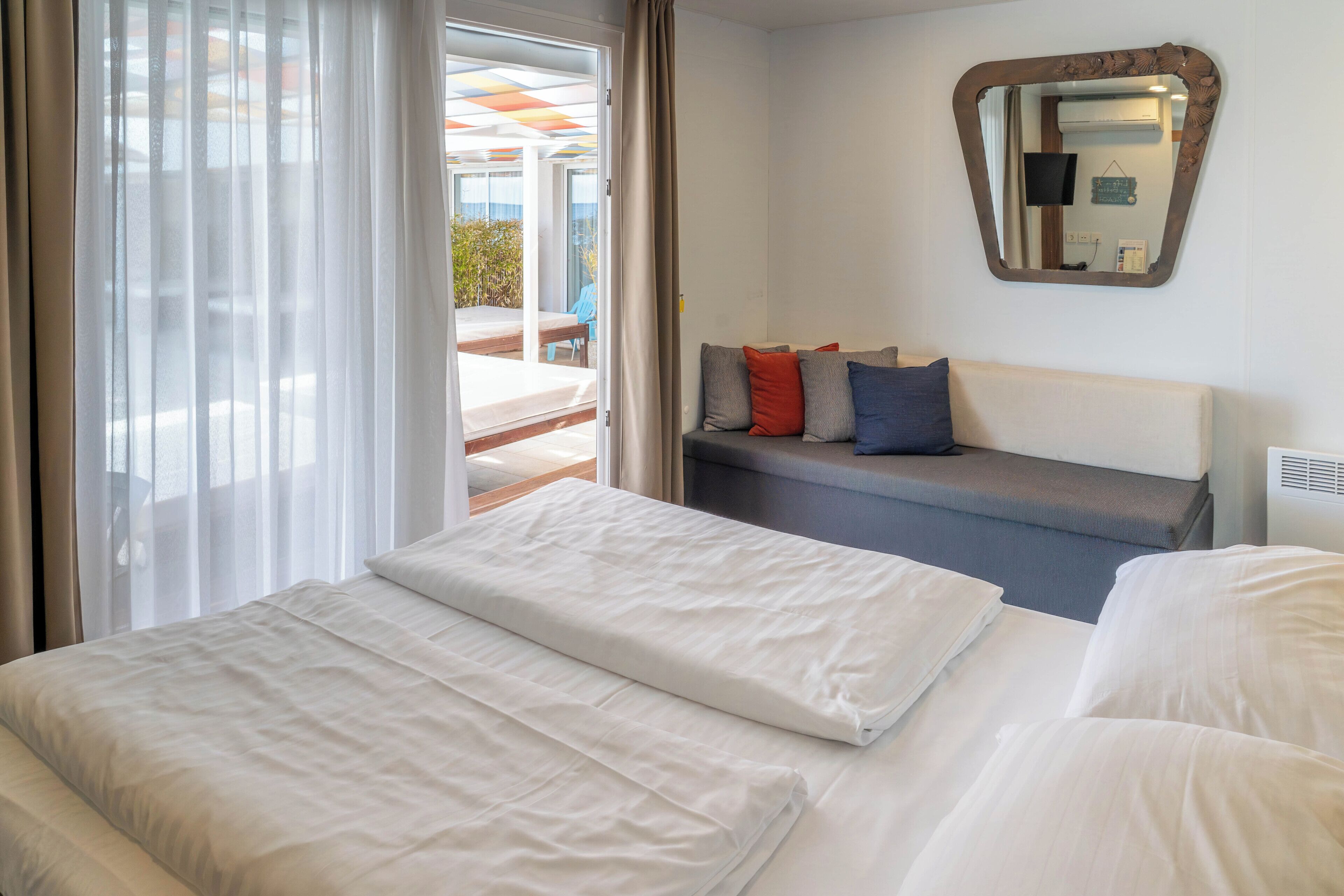A hotel room with a bed, a sofa, a mirror, and a view of the outdoor area.