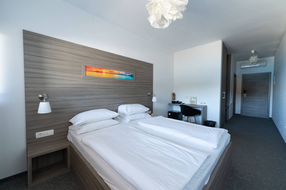 Une chambre d’hôtel moderne avec un grand lit, des tables de chevet, un bureau et un tableau au mur.
