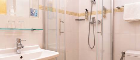 Un baño con cabina de ducha de vidrio, lavamanos blanco y retrete.