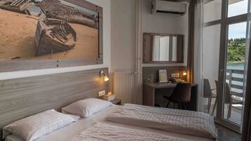 A hotel room with a large bed, a desk with a chair, a mirror, and a view of the sea through large windows.