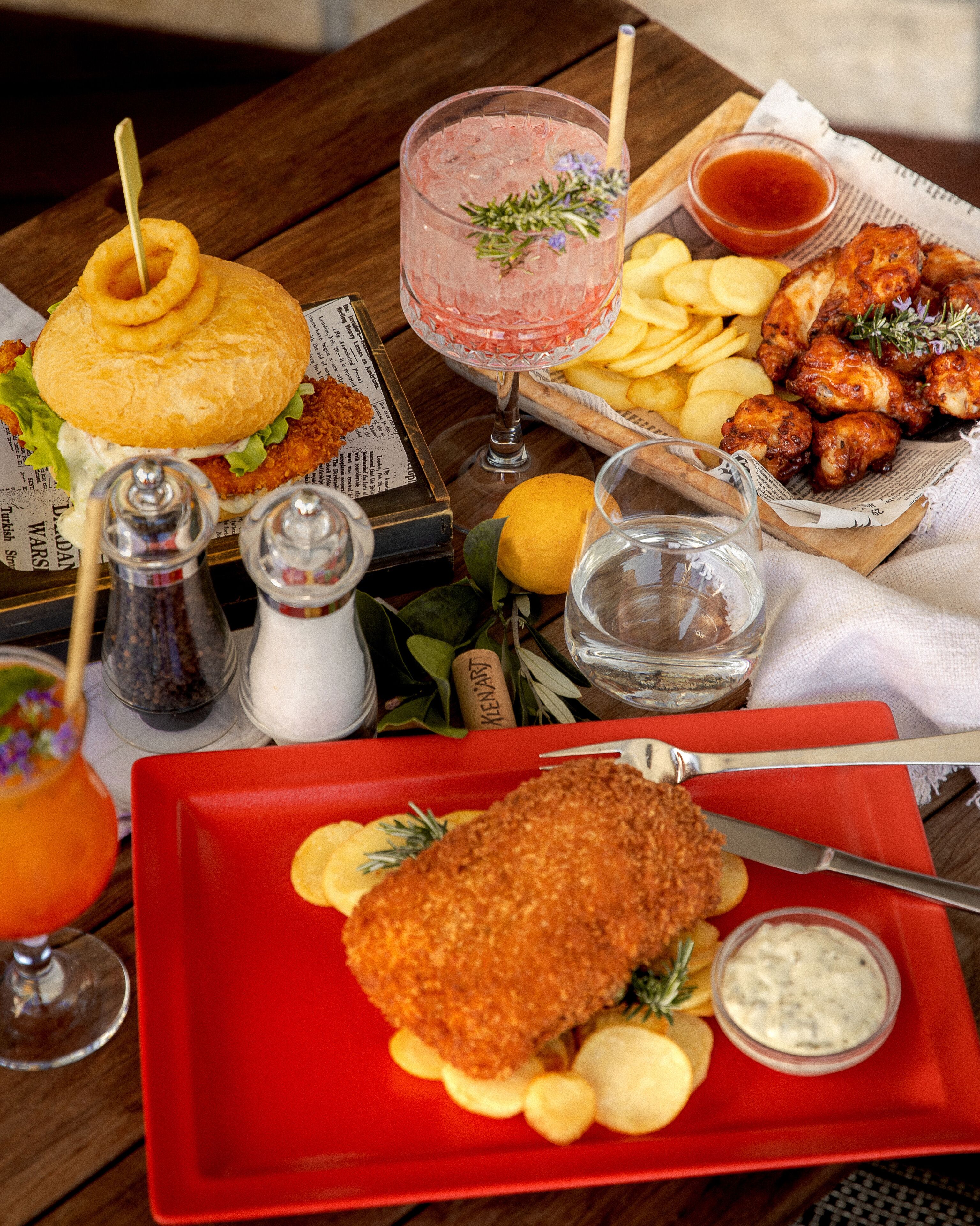A table with a variety of food items including a burger, fried chicken, fries, and a drink.