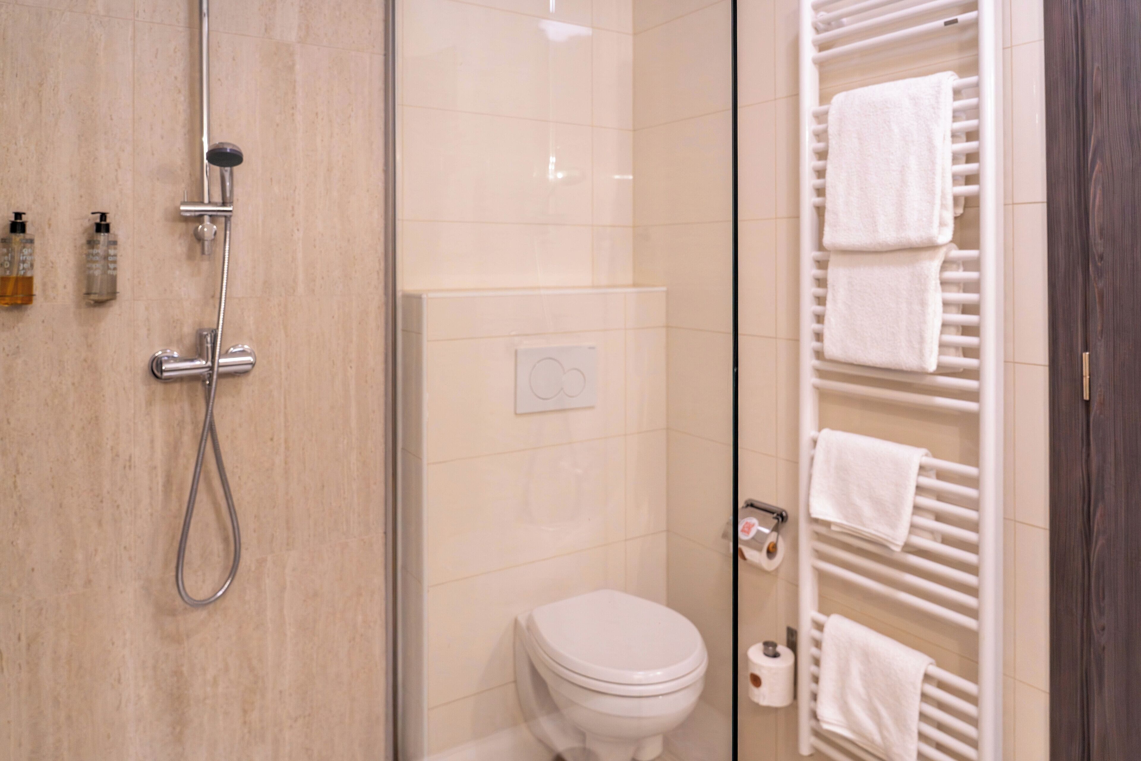 A bathroom with a glass shower enclosure, a toilet, and a towel rack with multiple towels.