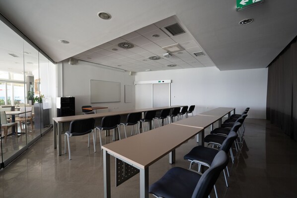 Una sala de conferencias con una larga mesa, sillas, una pizarra y una pantalla para proyector.