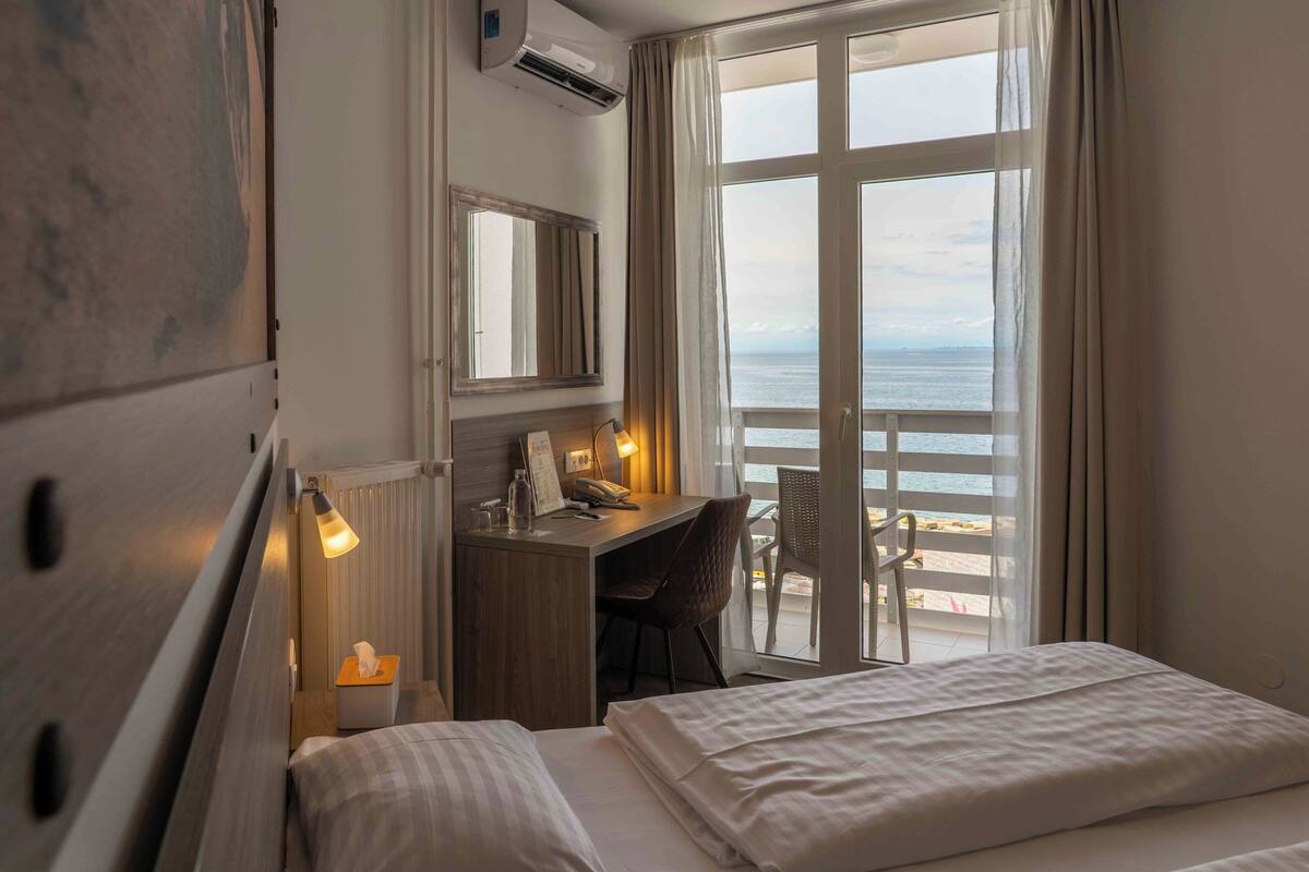 Une chambre d’hôtel équipée d’un lit, d’un bureau, d’une chaise, d’une fenêtre donnant sur la mer et d’un appareil de climatisation.