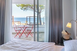 Habitación de hotel con cama, una mesa con sillas, vista al mar y un balcón con mesa y sillas.