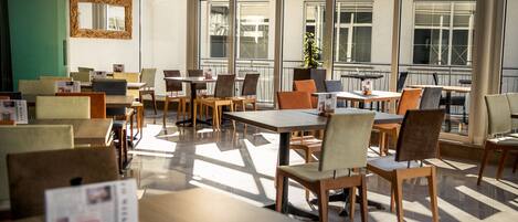 A modern dining area with tables and chairs, large windows, and a view of the outside.