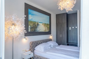 Un dormitorio con una cama, un cuadro de una playa, un armario y una lámpara de pie.