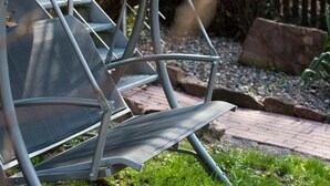 Outdoor metal chairs with a mesh seat and backrest, arranged on a paved area with grass and a stone border. - Hermann's Neue Post (Calw)