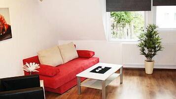 A cozy living room with a red sofa, a white coffee table, and a potted plant.
