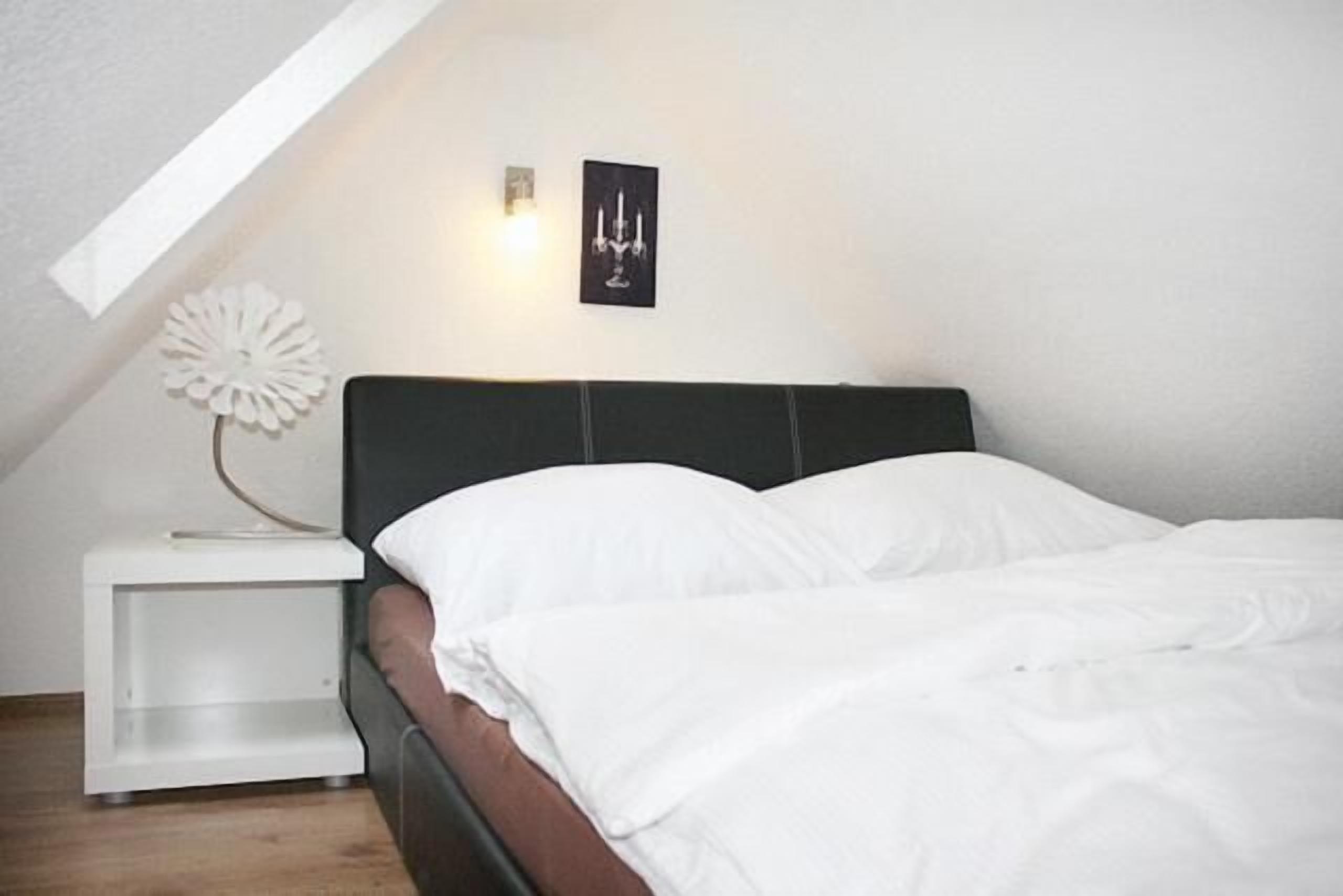 A bedroom with a bed, white nightstand, and a wall-mounted light fixture.