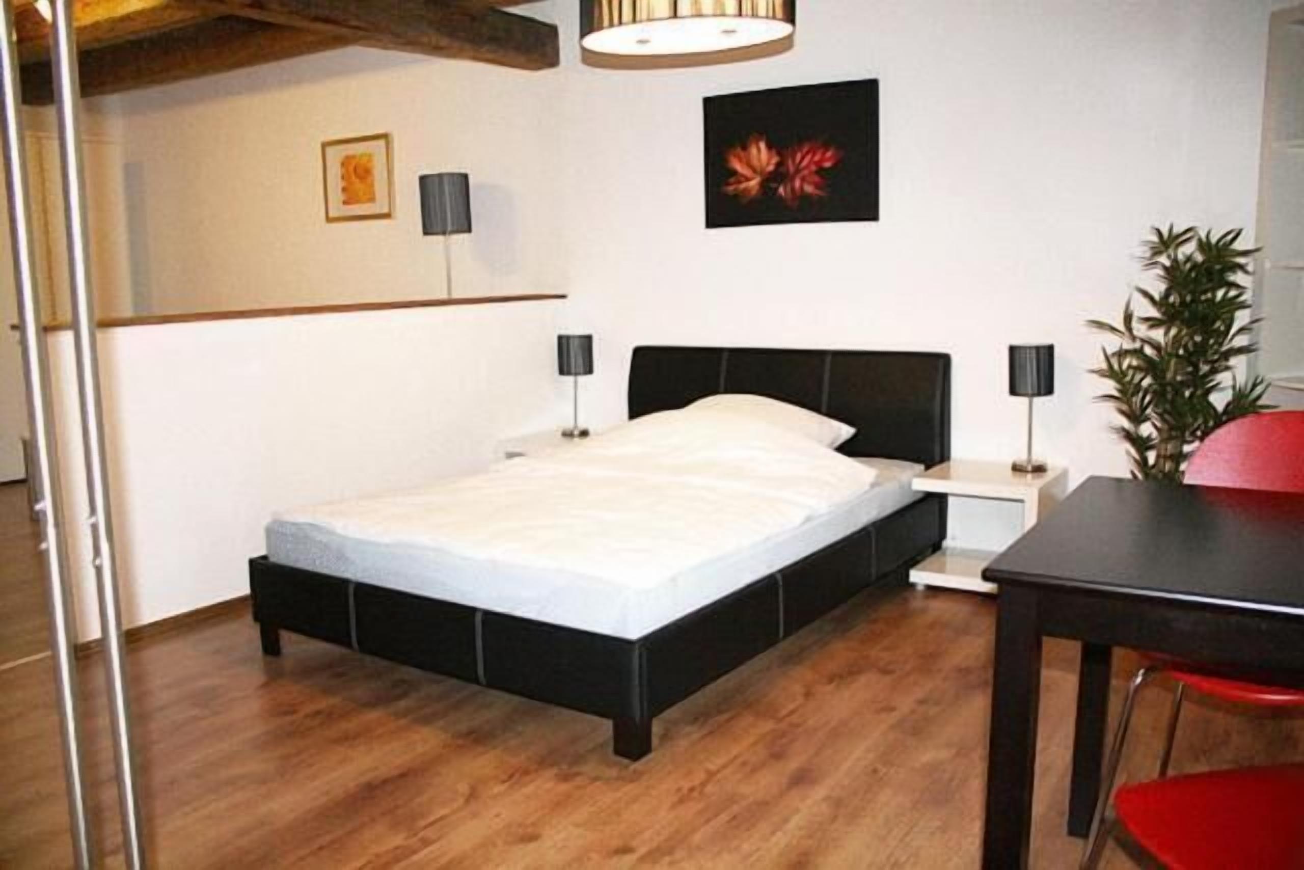 Un dormitorio con cama, mesitas de noche, una butaca roja y una planta en maceta.