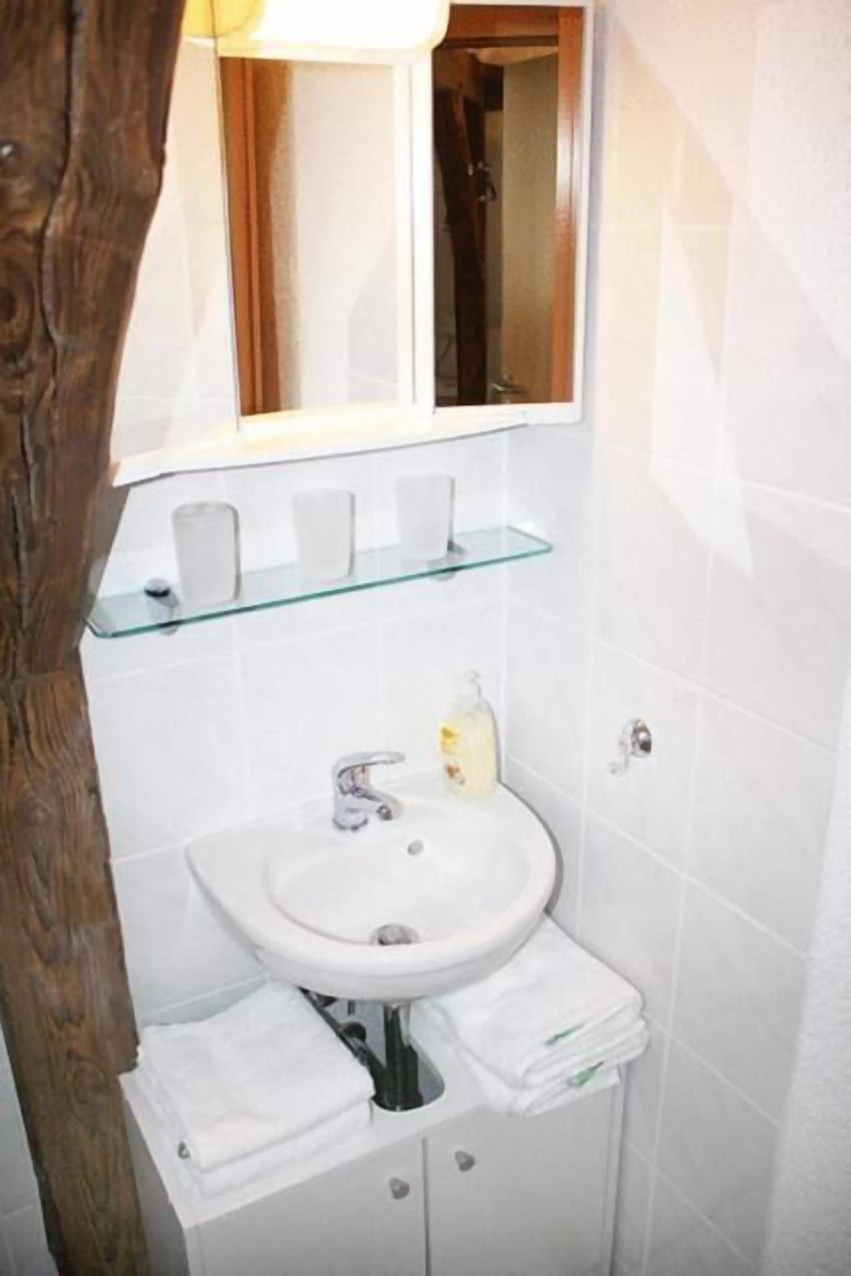 Un baño con un lavamanos blanco, una repisa de vidrio y un espejo encima.