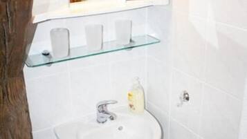Un baño con un lavamanos blanco, una repisa de vidrio y un espejo encima.