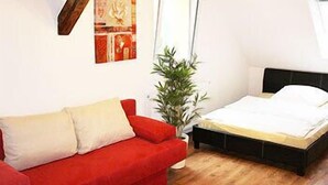 A room with a red sofa, a bed, a floor lamp, and a wall with a framed picture. - Hermann's Neue Post (Calw)
