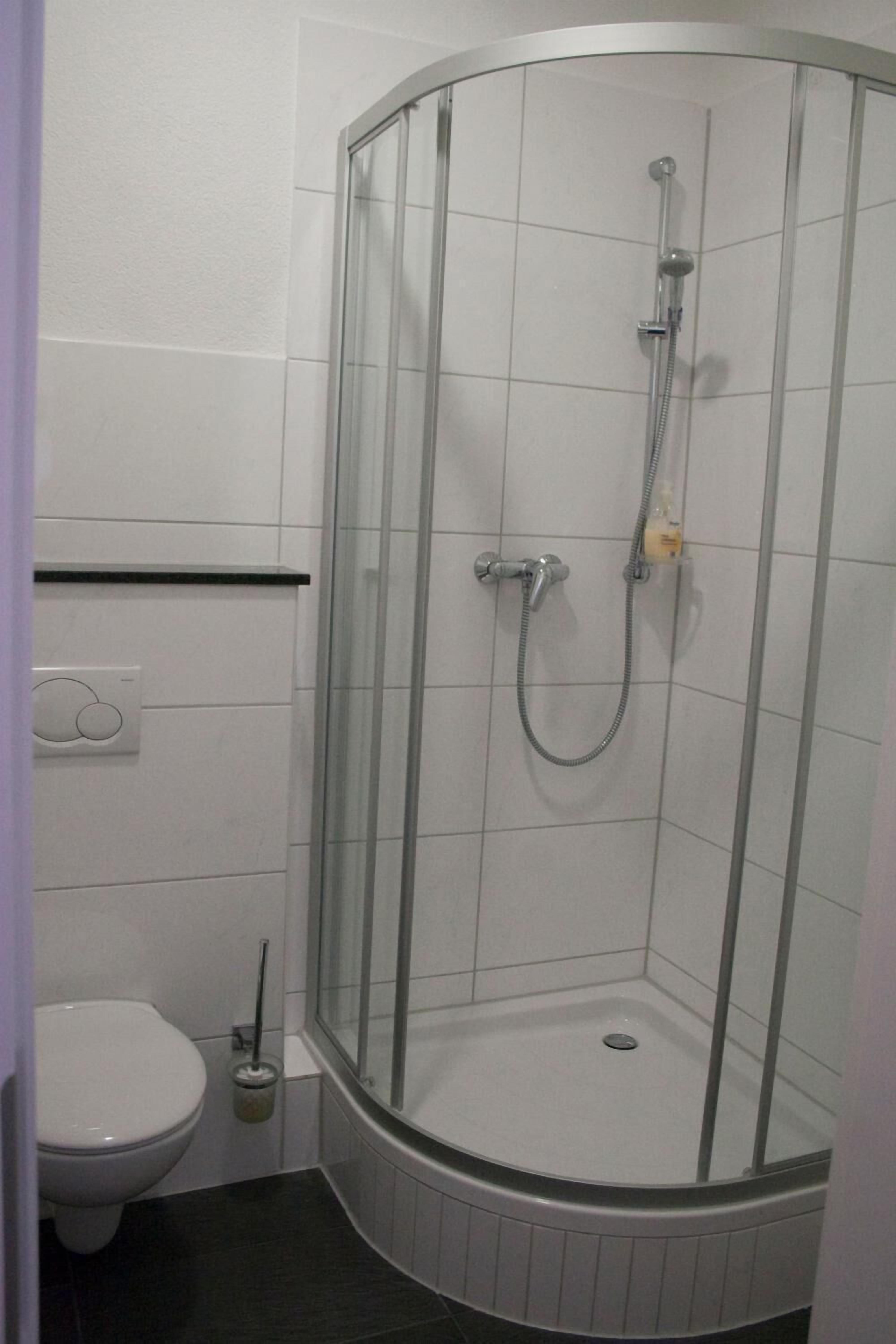 A corner shower with a glass door, a toilet, and a small trash bin.