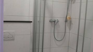A corner shower with a glass door, a toilet, and a small trash bin.