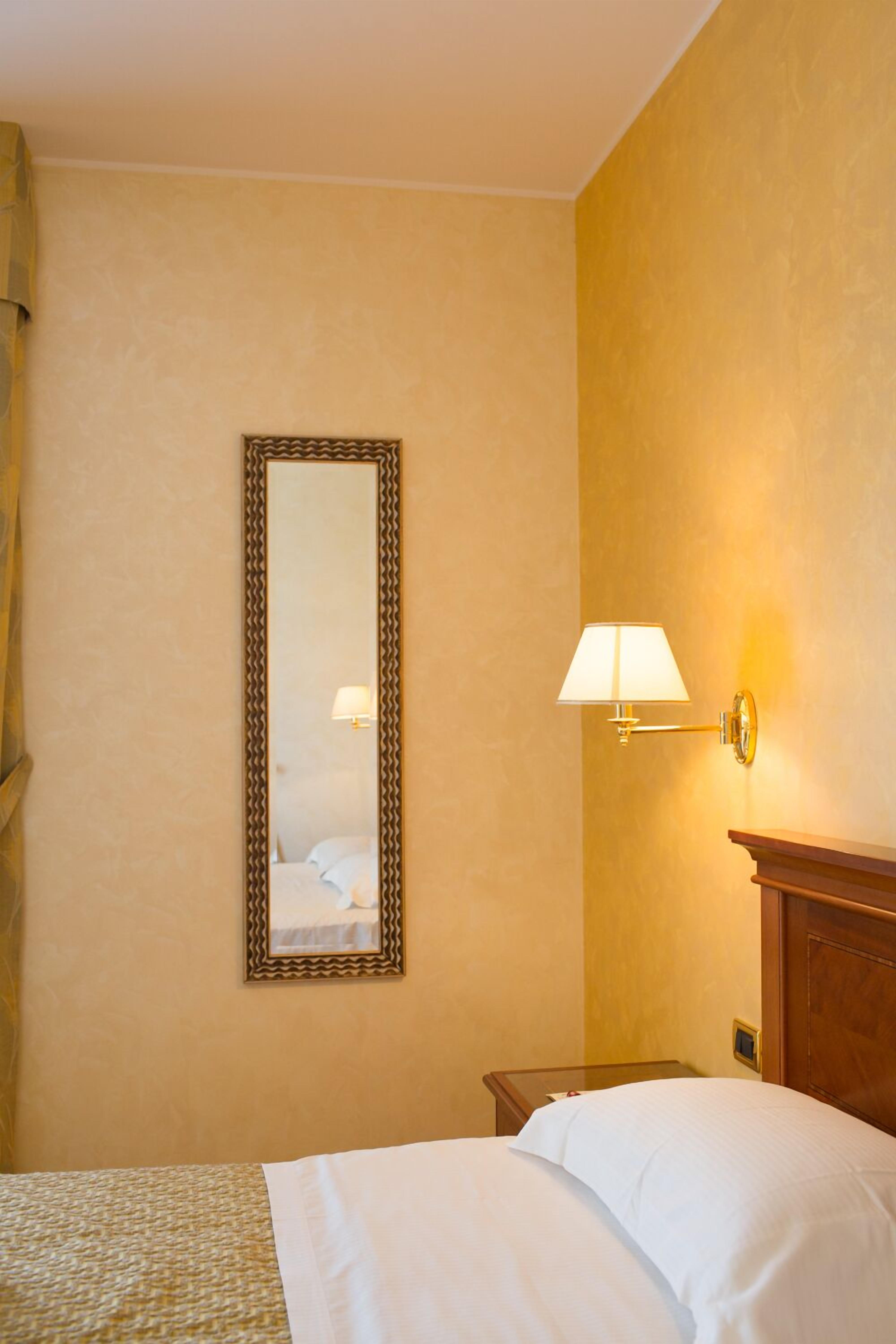 Una habitación de hotel con una cama, una mesita de noche, una lámpara de pared y un espejo.