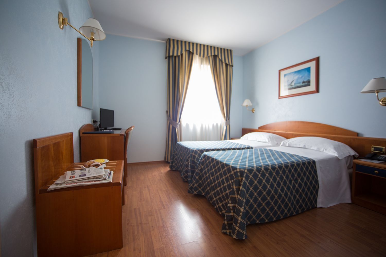 A hotel room with two beds, a desk, a chair, a TV, and a window with curtains.