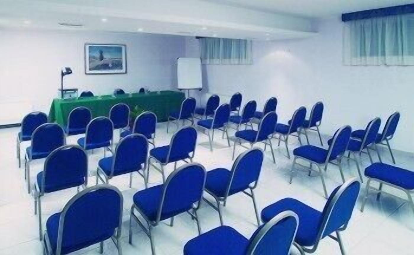 A conference room with rows of blue chairs, a whiteboard, and a green table.