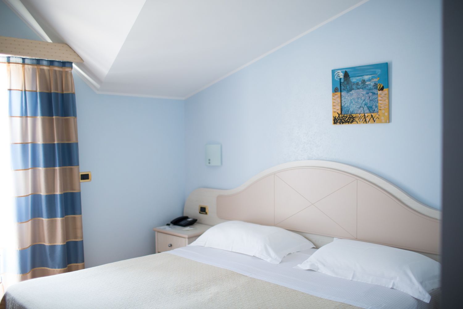 A hotel room with a bed, a nightstand, a telephone, and a painting on the wall.