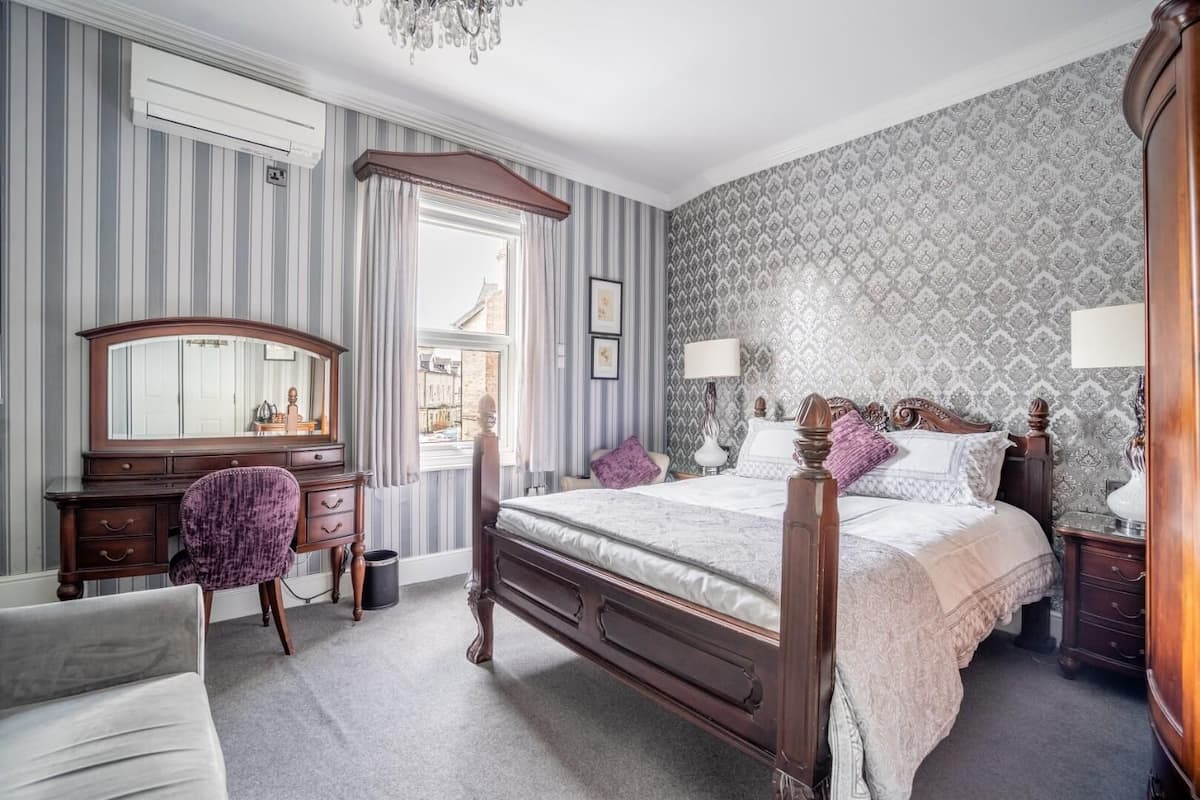 A bedroom with a four-poster bed, a dresser, a vanity, and a chair.