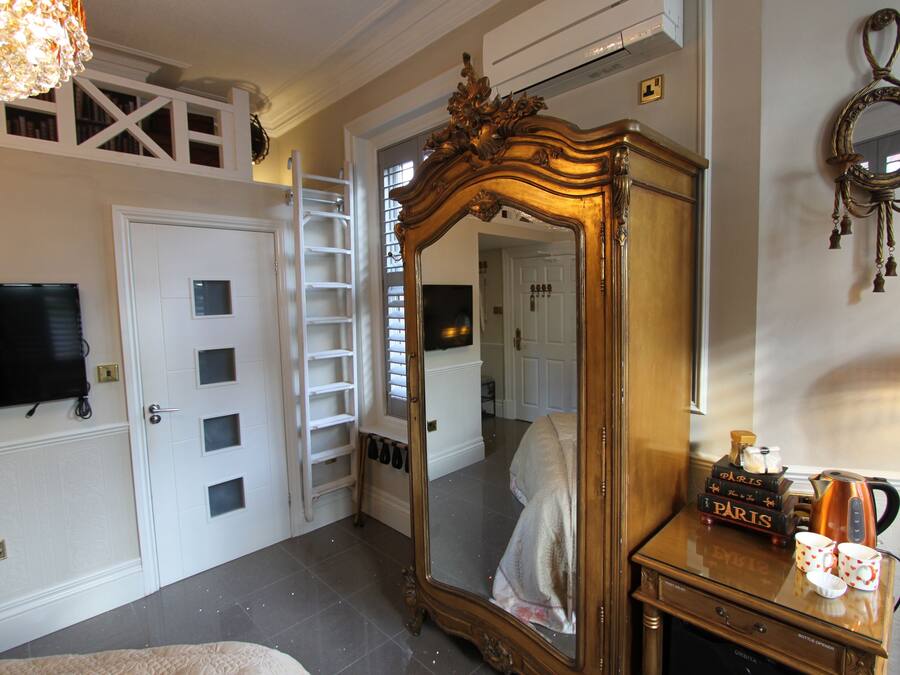 A bedroom with a large mirror, a wardrobe, a television, and a ladder.
