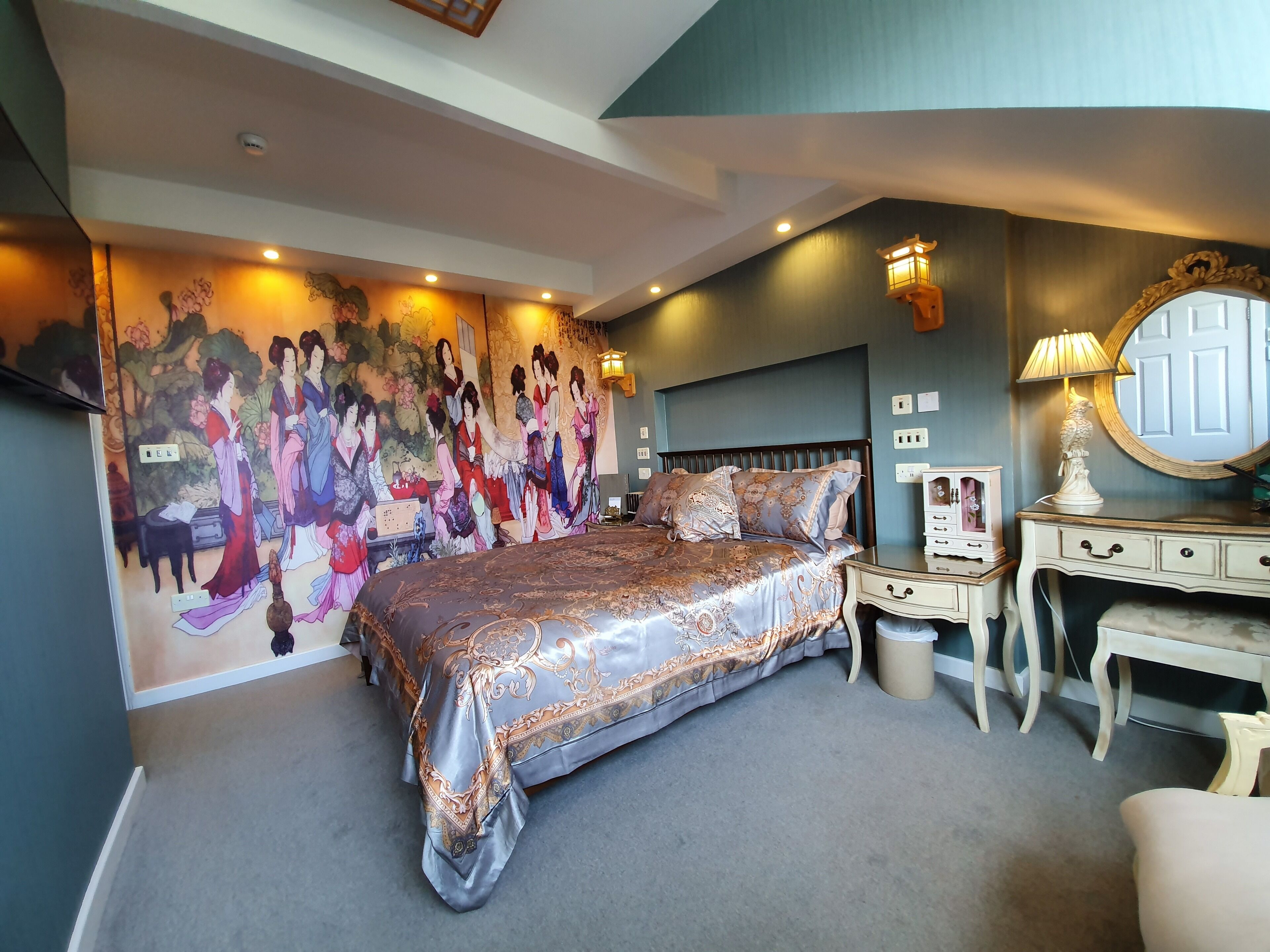 A bedroom with a large bed, a nightstand, a dresser, and a wall mural.