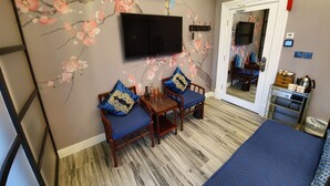 A room with a TV mounted on the wall, a wooden dining table with chairs, a bed, and a small table with a kettle and cups. - Tower Guest House (York)