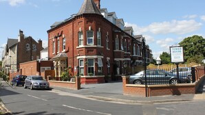 A red brick building with a tower, a sign indicating private parking, and a gated entrance. - Tower Guest House (York)