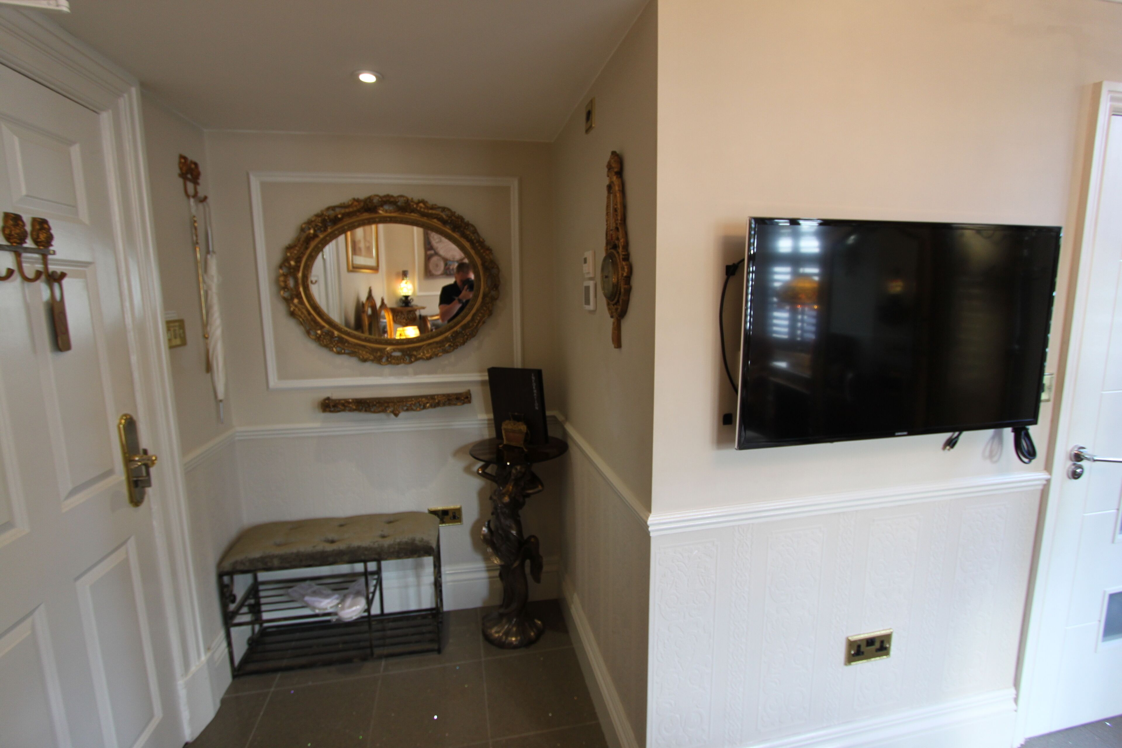 A hallway with a bench, a mirror, and a mounted television.