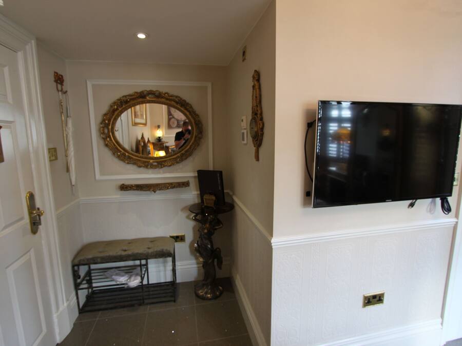 A hallway with a bench, a mirror, and a mounted television.