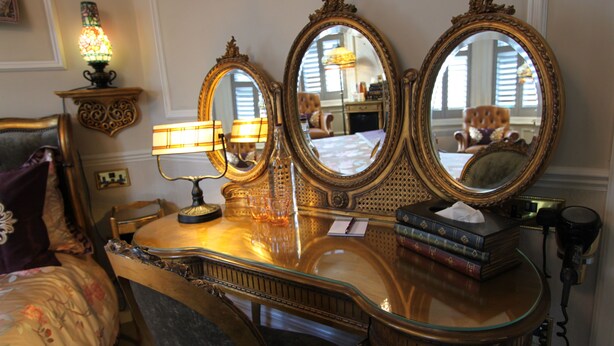 A vanity with three mirrors, a lamp, and a tissue box on a wooden vanity. - Tower Guest House (York)