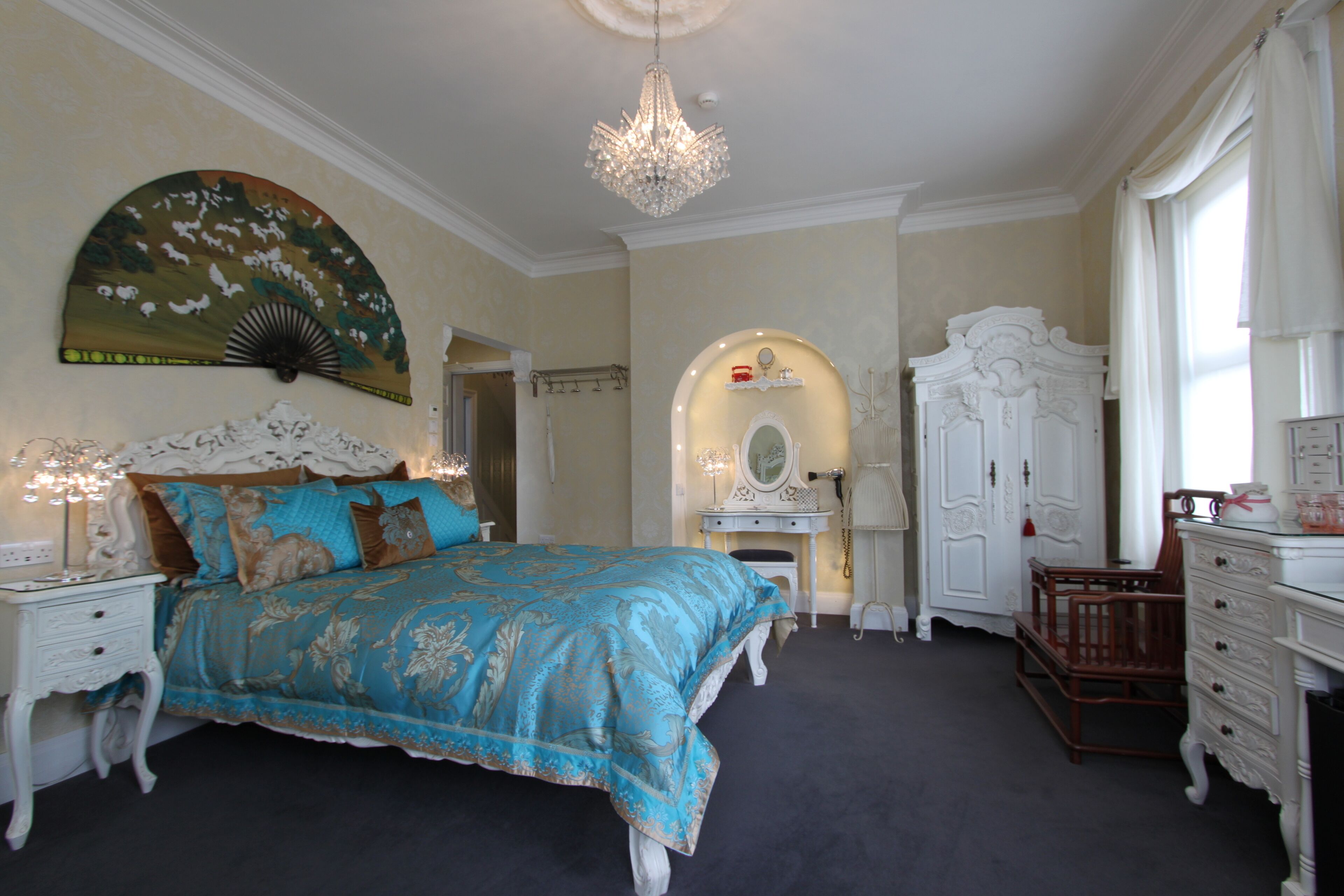 A bedroom with a large bed, a chandelier, a vanity with a mirror, and a wardrobe.