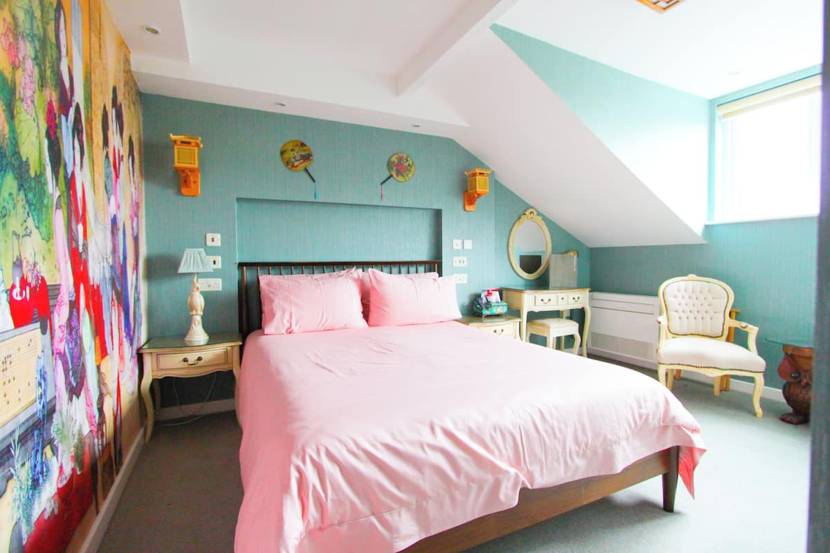 A bedroom with a bed, a nightstand, a dresser, a chair, and a wall with artwork.