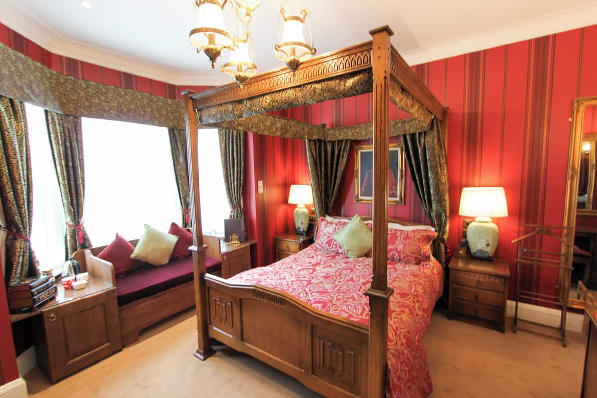 A four-poster bed with a canopy, a bedside table with a lamp, and a mirror on the wall.