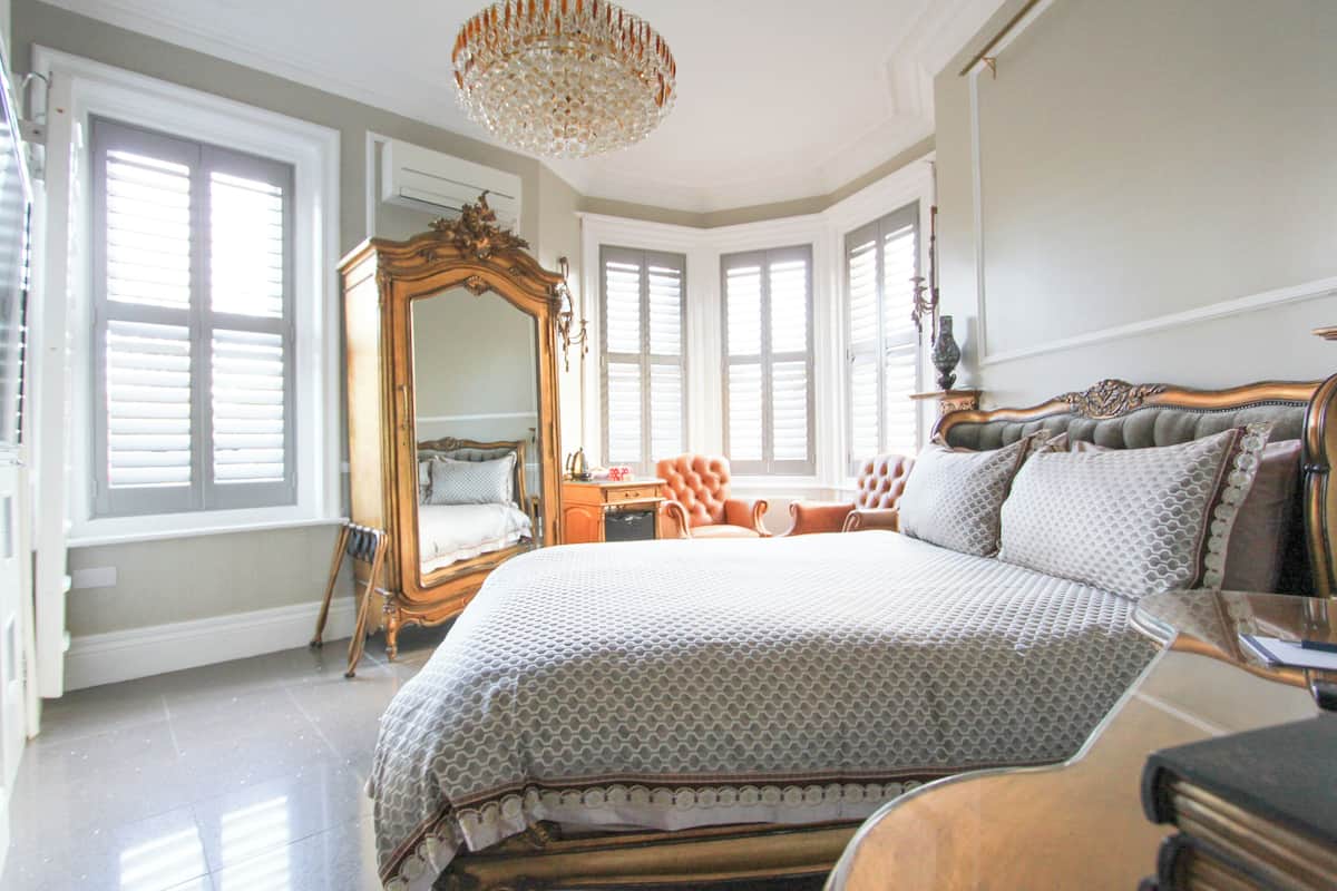 A bedroom with a large bed, a mirror, a chaise lounge, and a chandelier.