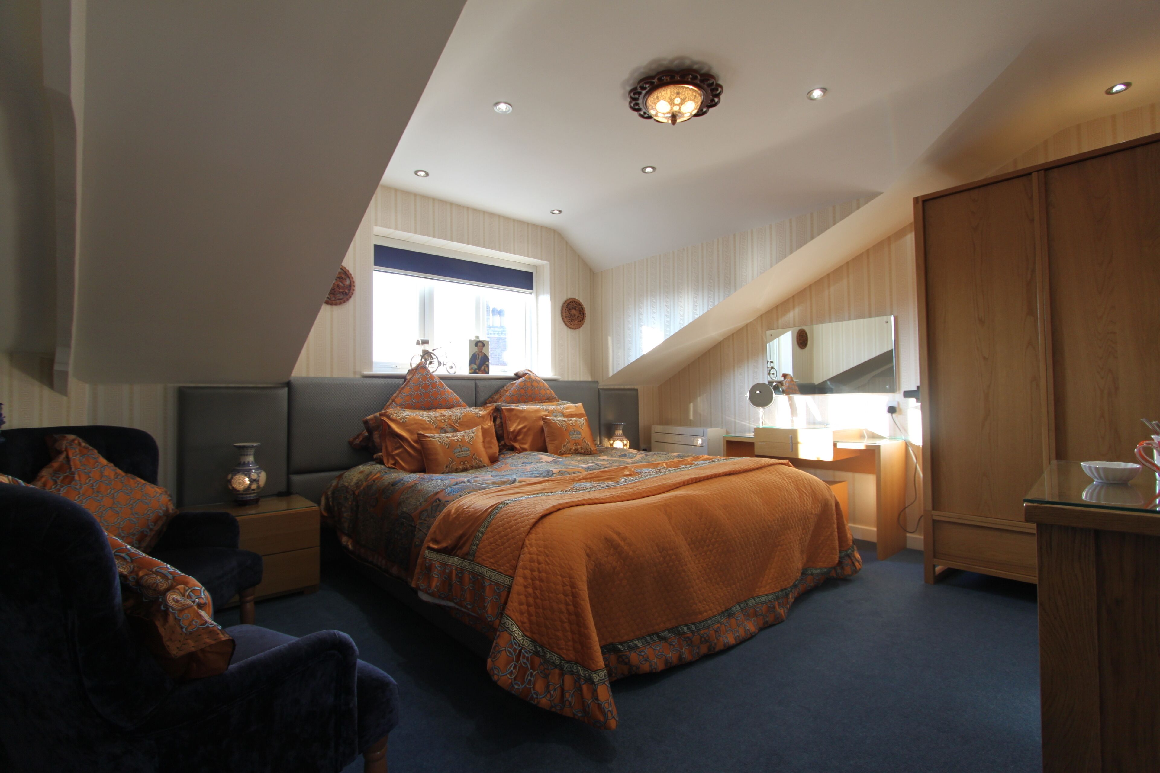A bedroom with a large bed, a nightstand, a dresser, and a window with blinds.