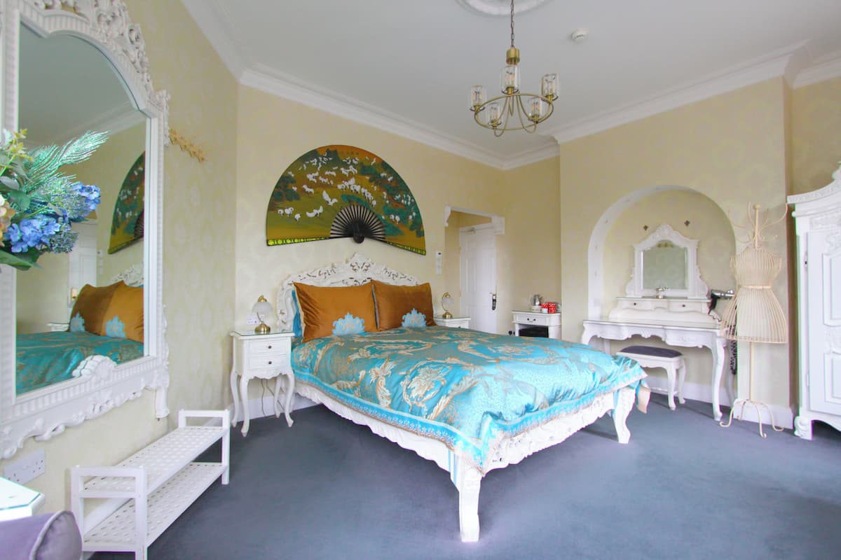 A bedroom with a large bed, a vanity, a mirror, and a chandelier.