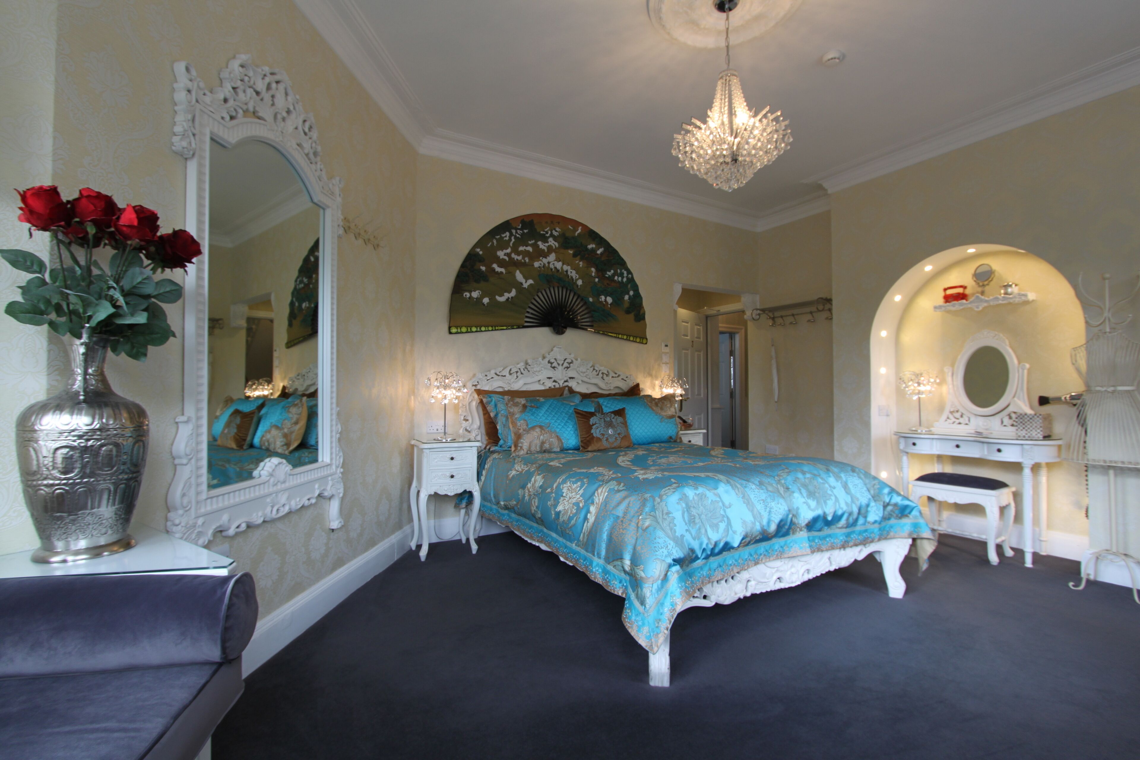 A bedroom with a bed, a vanity with a mirror, and a chandelier.