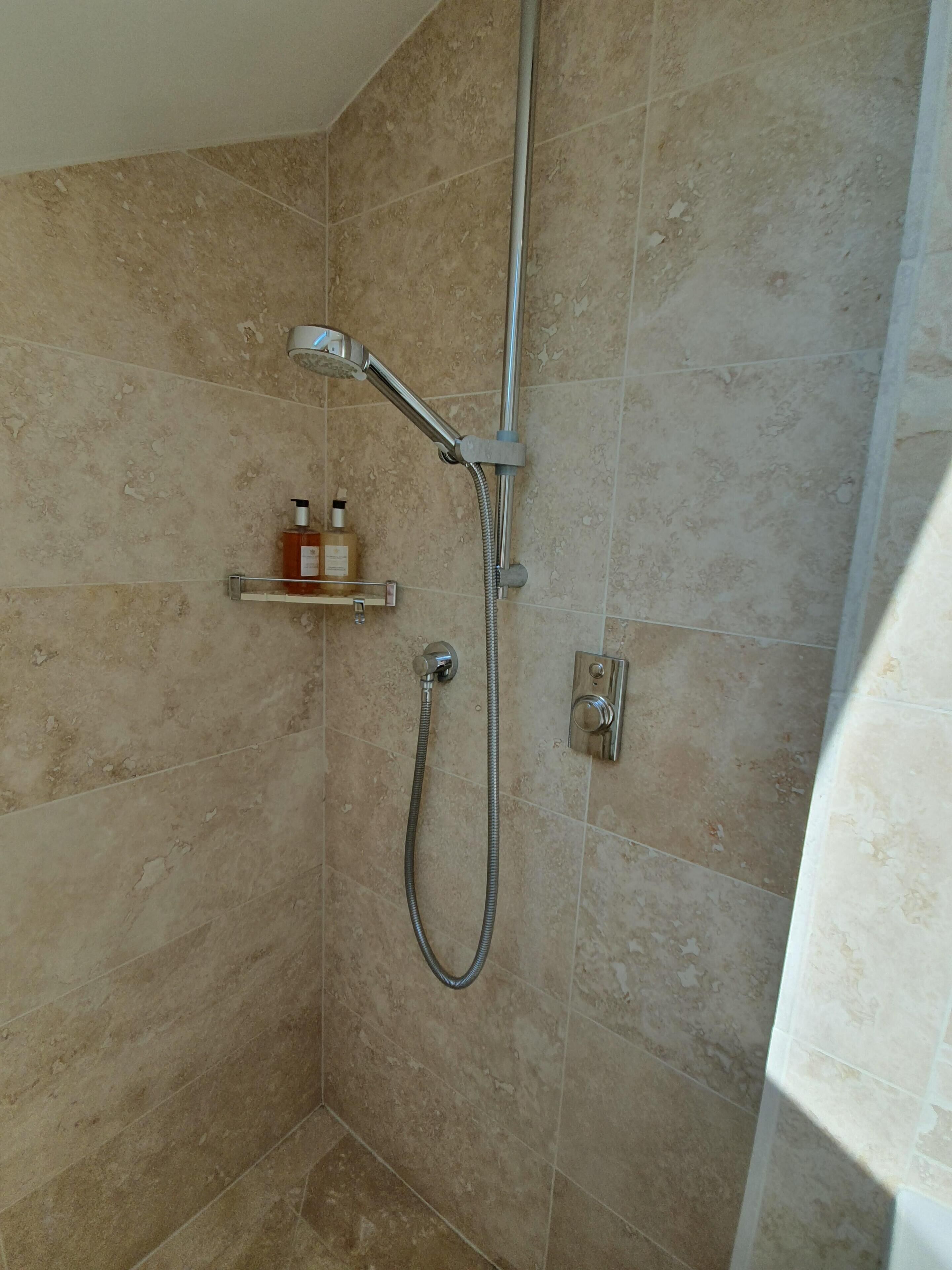 A shower area with a handheld showerhead and a wall-mounted faucet. There is a shelf with toiletries.